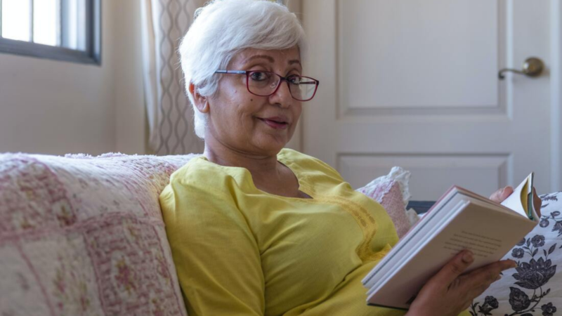 An older woman with white hair sits on a couch studying