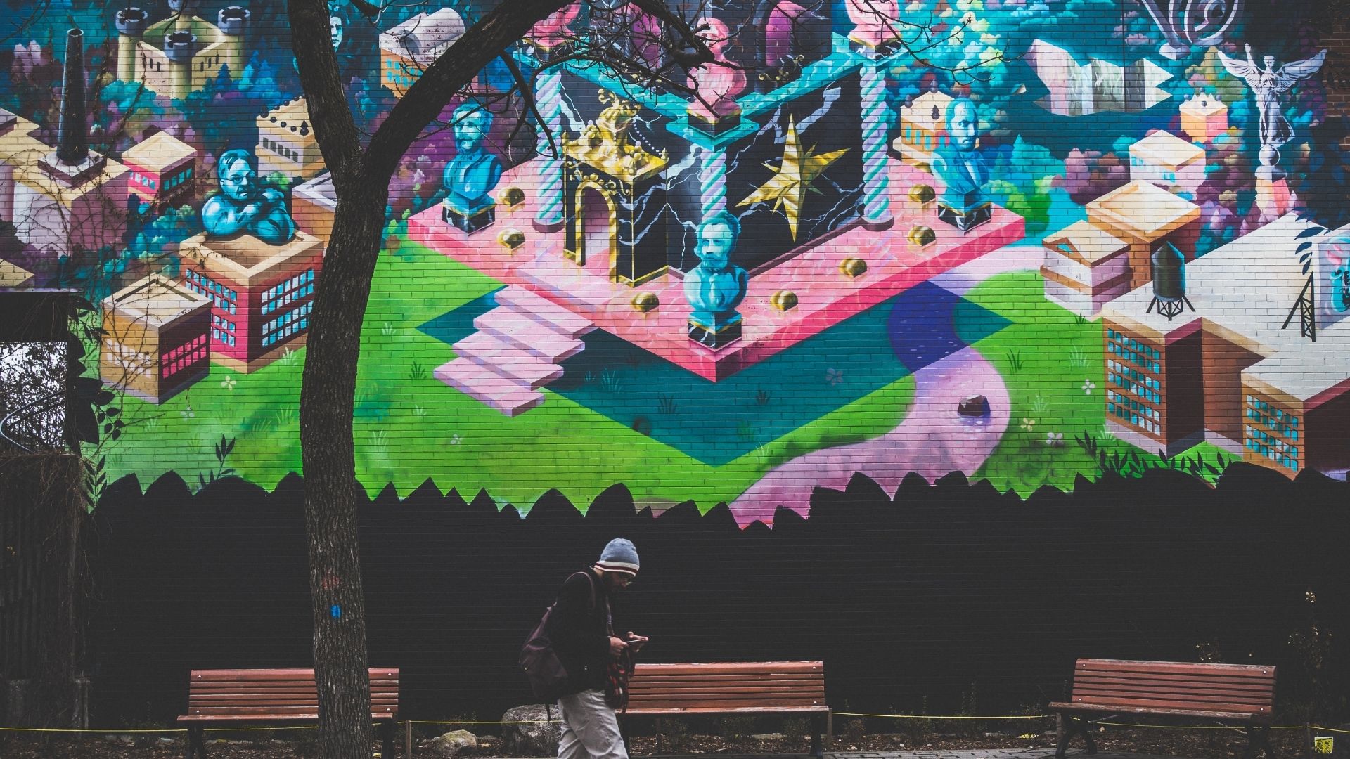 A lone tour guest is on their phone underneath a large street mural.